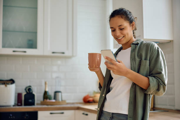 istock Happy Hispanic woman using cell phone while drinking coffee in the kitchen. 2177584393
