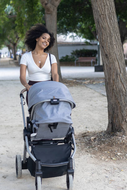 istock Young mother smiles while pushing her baby in a stroller through a tree-lined park path 2177610048