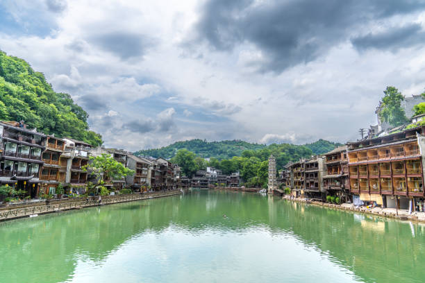 English description: Traditional Miao architecture by the river in Fenghuang Ancient Town, surrounded by greenery and hills.