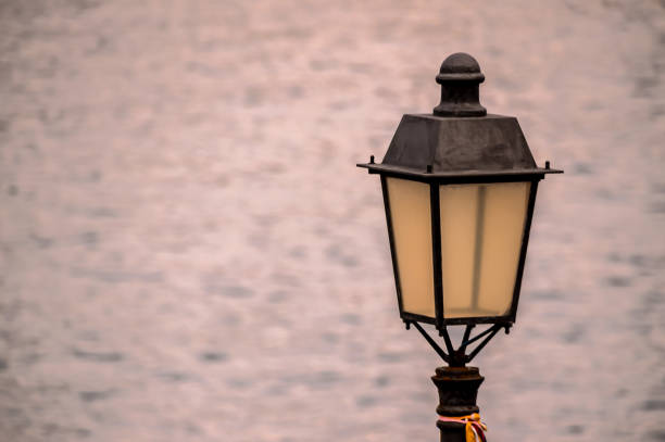 A lamp post is lit up by the water, creating a serene and peaceful atmosphere. The lamp post is positioned on the edge of the water, with the water appearing calm and still