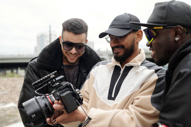 Three men gathered around professional camera, sharing smiles while reviewing footage. Group showing interaction and collaboration during outdoor filming session