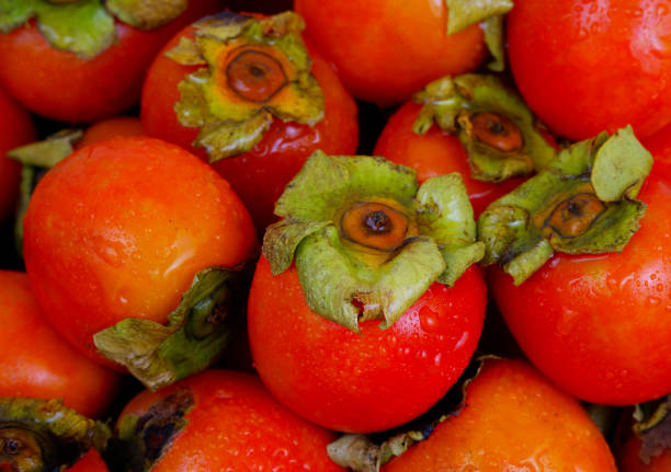 Wet whole and sliced persimmon fruits close up.