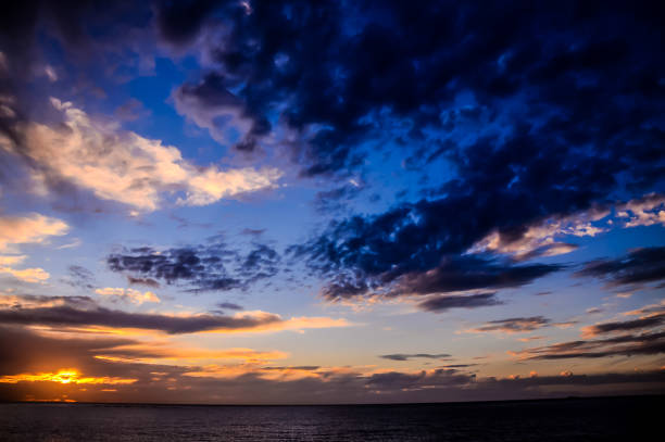 The sky is a beautiful blue with a few clouds. The sun is setting and the water is calm