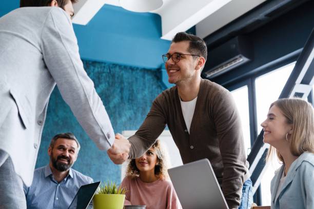 istock Welcome on board. Confident men shaking hands and smiling while sitting at the desk in office 2177657597