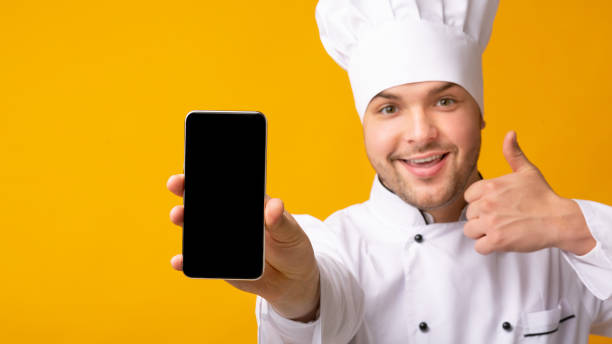 istock Male Chef Showing Smartphone Screen Gesturing Thumbs-Up Over Yellow Background 2177661604