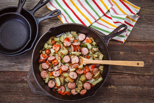 Sliced smoked sausage, potatoes, bell peppers, onions and tomatoes in a cast iron skillet.