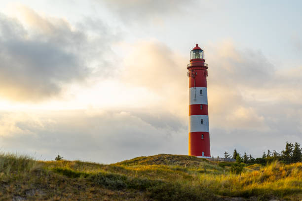 istock A striking red and white lighthouse stands tall against a colorful sunset sky, surrounded by rolling hills and lush greenery 2177674908