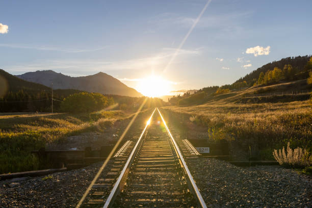 View down train tracks to sunrise over mountains, Canadian Rockies