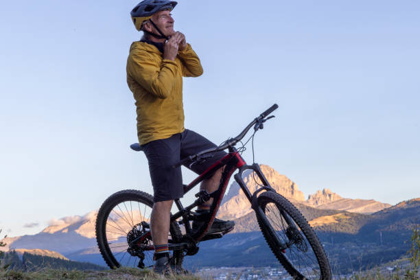 istock Mature mountain biker puts on helmet at sunrise 2177680079