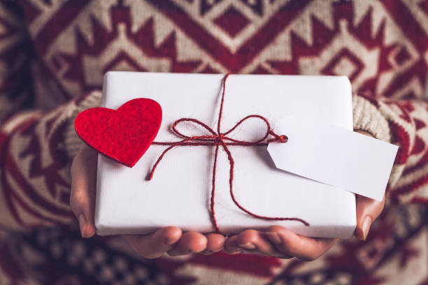 istock Hands hold, give a gift packed in white paper with felt heart and Greeting label 2177680930