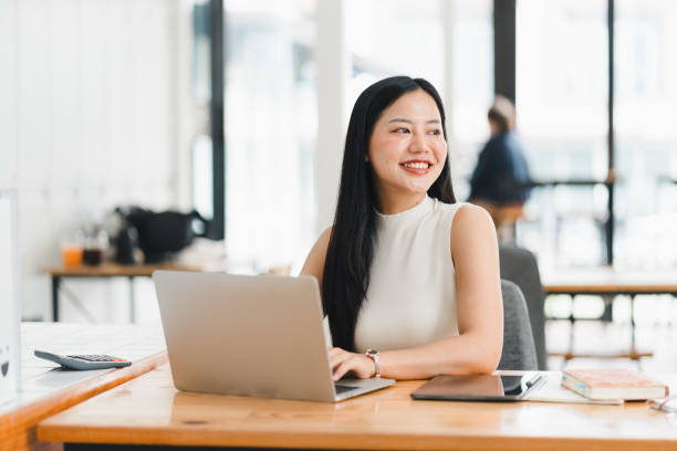 istock A young woman smiles while working on laptop in modern office. 2177683907
