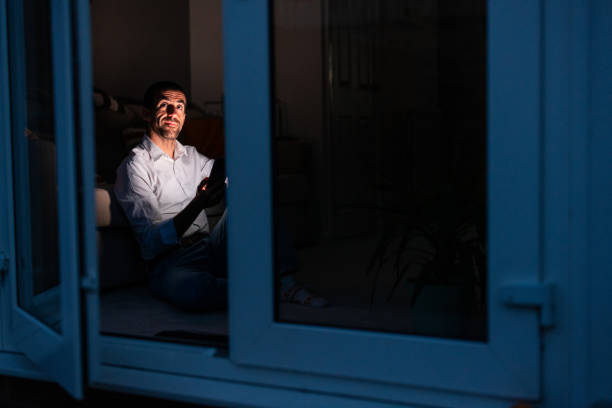 Man using smartphone at night sitting on floor by window