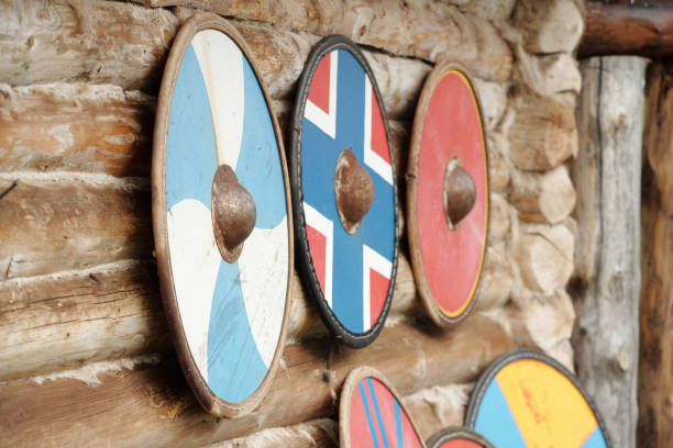 Several Viking shields are hanging on a rustic wooden wall. Each shield displays unique designs, showcasing various colors and patterns