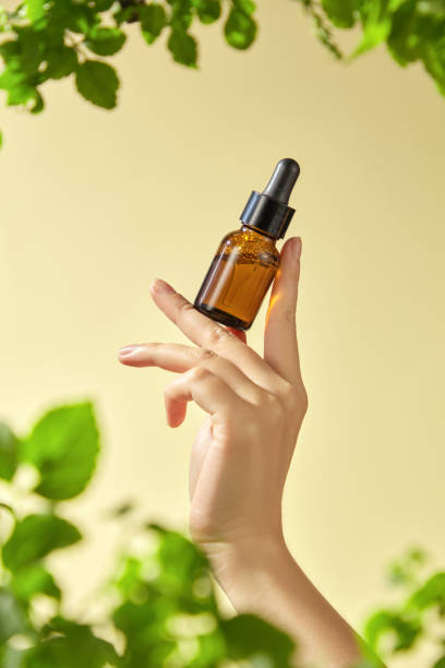 istock The image features a hand delicately holding a brown glass bottle with a dropper mockup, containing an essential inside. The yellow background and surrounding green foliage. 2177691926