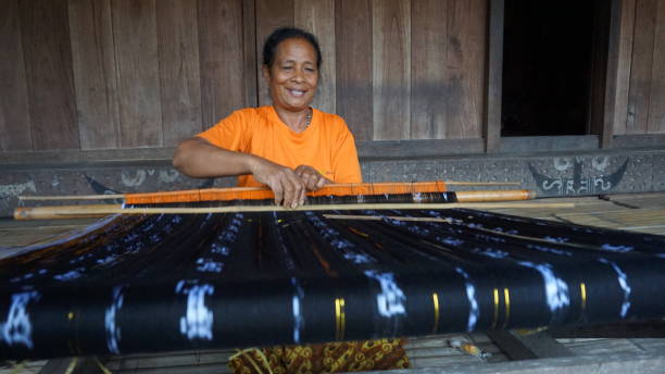 Bena Village, 17 May 2017: a woman is weaving cloth in front of a traditional house