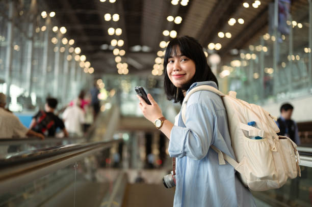 istock Happy young woman with backpack using mobile phone while on escalator in an airport terminal 2177713011