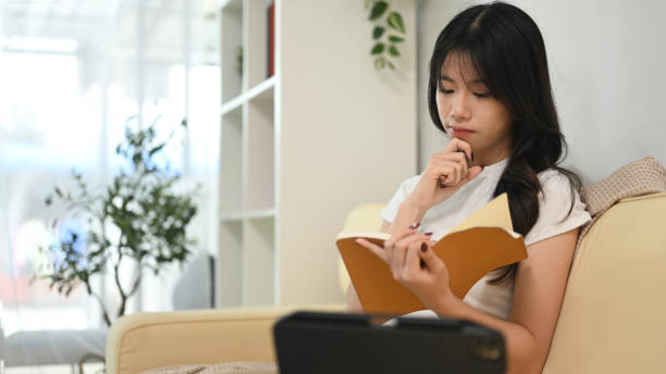istock Peaceful young woman sitting on beige sofa and reading book 2177713063