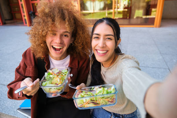 Cheerful college students taking a selfie while eating salad