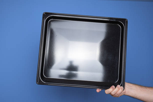 istock Empty, black, rectangular shallow baking tray. Held by hand by Caucasian male hand. Close up studio shot, isolated on blue 2177728142