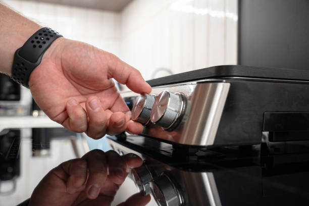 Close-up of a male hand turning an electric grill knob at modern kitchen. The image highlights the sustainable energy and daily routine in cooking or kitchen maintenance.