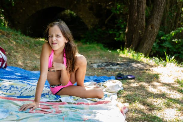 Two teenage girl friends are lying on the grass by the river and sunbathing. Their dog is sitting next to them. They are having a relaxing time.