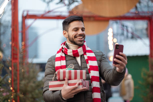 istock A joyful man holding gifts and using a smart phone outdoors 2177742754