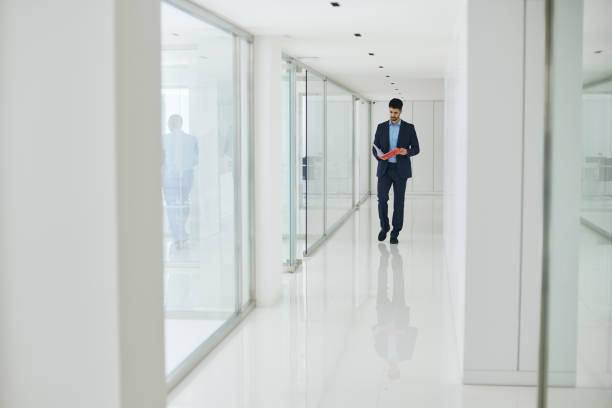 istock The man walks into the office, reading documents, moving through the corridor featuring glass walls. 2177742803