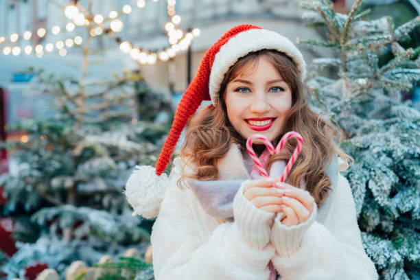 istock Young smiling woman in Santa hat making heart shape with candy canes while walking on traditional street Christmas market. Happy New Year celebration Christmas holidays. Share love, charity concept. 2177776581