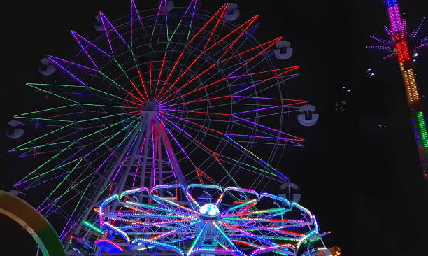 istock Vibrant night scene at an amusement park with a large Ferris wheel illuminated by multicolored lights and bright neon shades carousels. Festive atmosphere conceptual background 2177777285