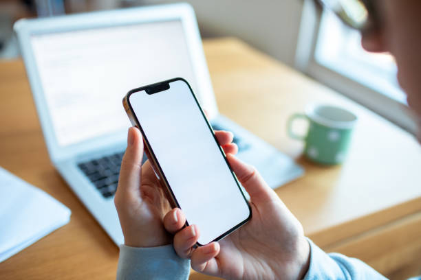 istock Young woman using a phone while studying or working on her laptop at home 2177781547