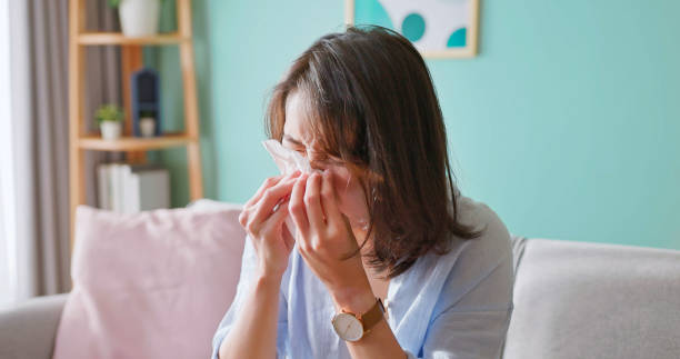 asian woman sitting on couch is sick and sneezing with tissue paper in living room at home