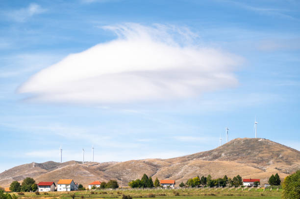 Wind turbines on a hill overlook agricultural fields below, where farming activities take place against a sustainable landscape