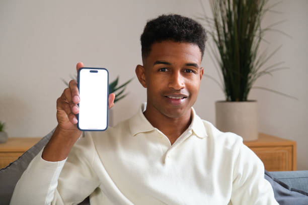 istock Young man sitting on sofa is showing smartphone with white screen 2177816659