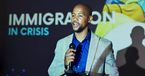 istock Seminar, speaker and black man at screen for global immigration with microphone, tablet and presentation. Ideas, change and presenter on stage for conference on international refugee crisis forum 2177825915