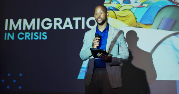 istock Seminar, presenter and black man at screen for global immigration presentation with microphone, tablet and ideas. Information, change and speaker on stage for conference on world refugee crisis forum 2177825922
