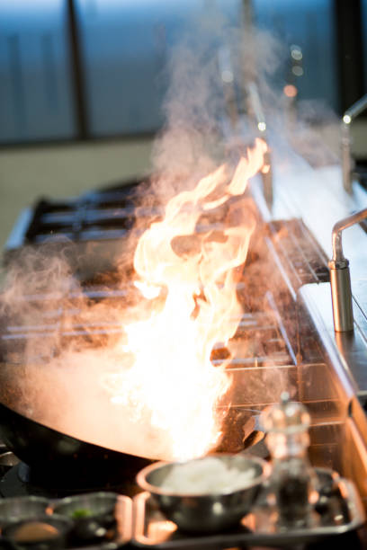 Chef in a kitchen and making flaming during making fried rice. Process of cooking over high heat in the flame of boiling oil on a gas stove in a cast iron frying pan, Asian cuisine.
