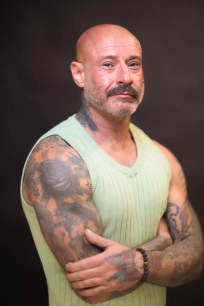 Tough-looking man of 48 wearing a sleeveless vest to show off his tattoos.