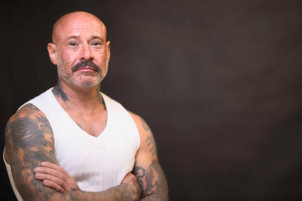 Tough-looking man of 48 wearing a white vest to show off his tattoos.