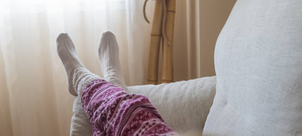 Relaxed Person On The Sofa Wearing Comfortable Clothes And Soft Wool Socks, Enjoying The Warmth In Their Apartment On A Cold Winter Day During Christmas.