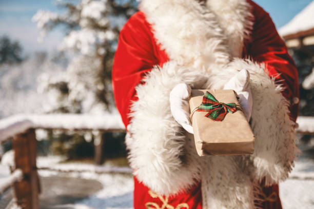 Santa Claus with gift box on Winter day outdoor delivering Christmas present. Copy space