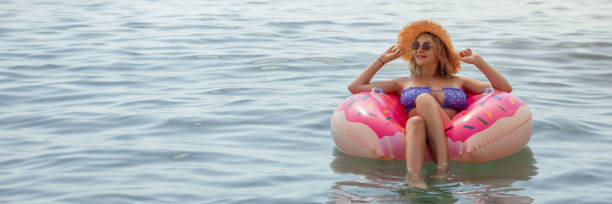 Beautiful young woman with inflatable donut in blue sea .