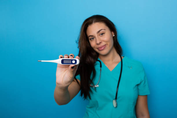 Young woman nurse in scrubs checking a patient's temperature with a thermometer