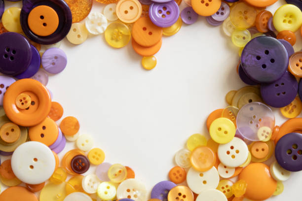 A collection of colorful buttons arranged in the shape of a heart on a white background. The buttons are in various shades of orange, yellow, purple, and white, creating a playful and creative design.