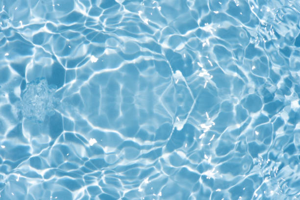 Blue water with ripples on the surface. Defocus blurred transparent blue colored clear calm water surface texture with splashes and bubbles. Water waves with shining pattern texture background.
