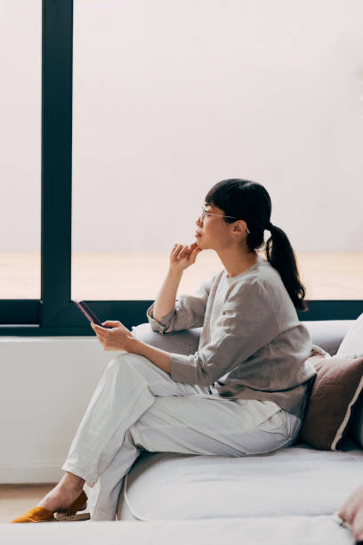 Pensive Woman Sitting on Couch Using a Digital Tablet