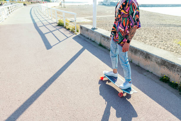 unrecognizable stylish skater in jeans and sneakers standing on skateboard in skatepark on sunny day in summer