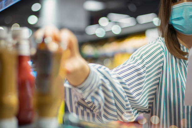 View of an almost unrecognizable woman behind the face mask and in stripped shirt, reaching for a dressing item placed on the shelf.