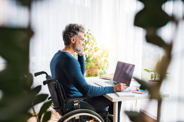 istock Handsome man in wheelchair working from home office, making phone call and writing notes in planner. Telecommuting and home office. 2177870857