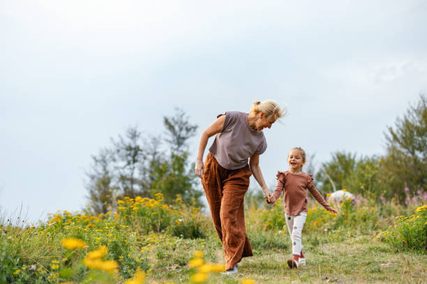 A joyful mother and daughter stroll hand in hand through a vibrant, sunlit meadow. The scene captures a moment of family connection and happiness in nature's beauty.