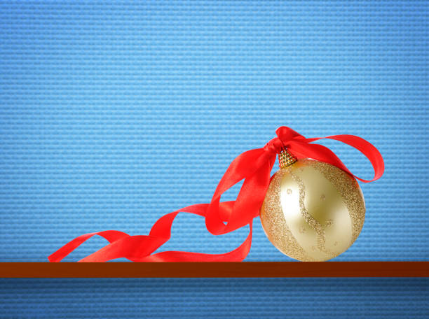 Christmas ball on a wooden shelf against light blue wall with copy space.